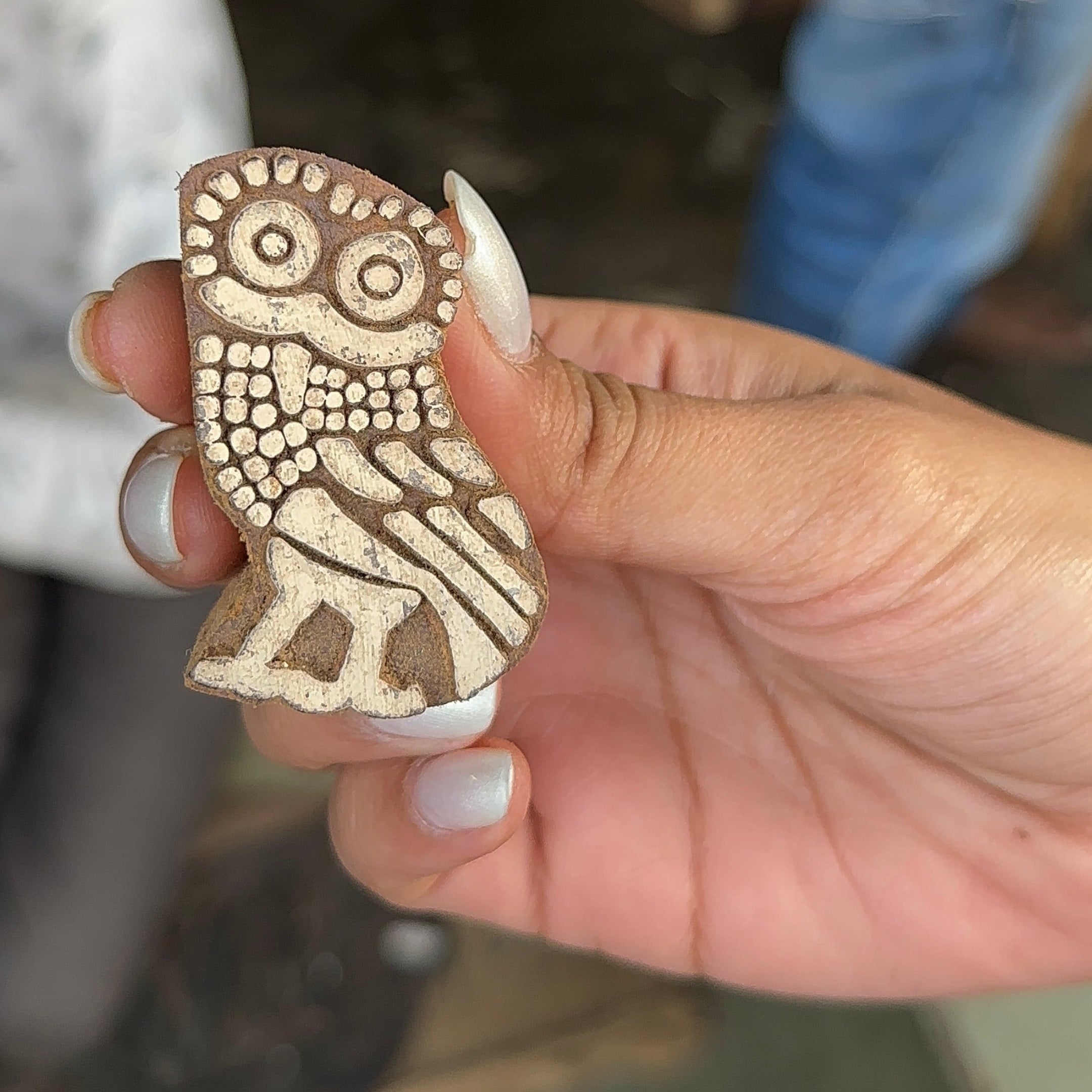 Hand holding a wooden stamp with an owl design in a workshop setting