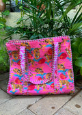 Pink bag with tiger pattern on a stone surface with plants in the background