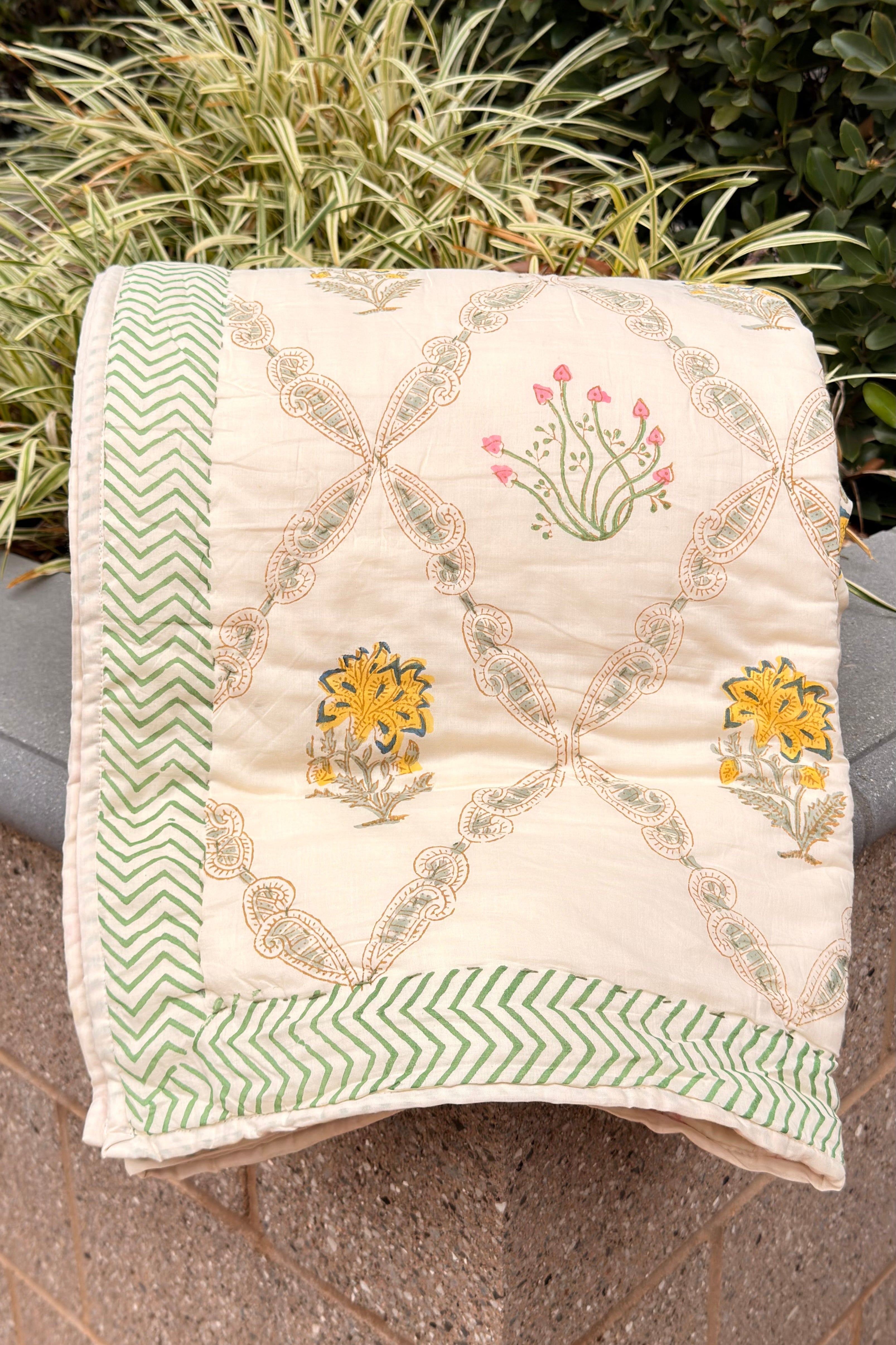 Embroidered quilt with floral patterns on a stone surface with greenery in the background