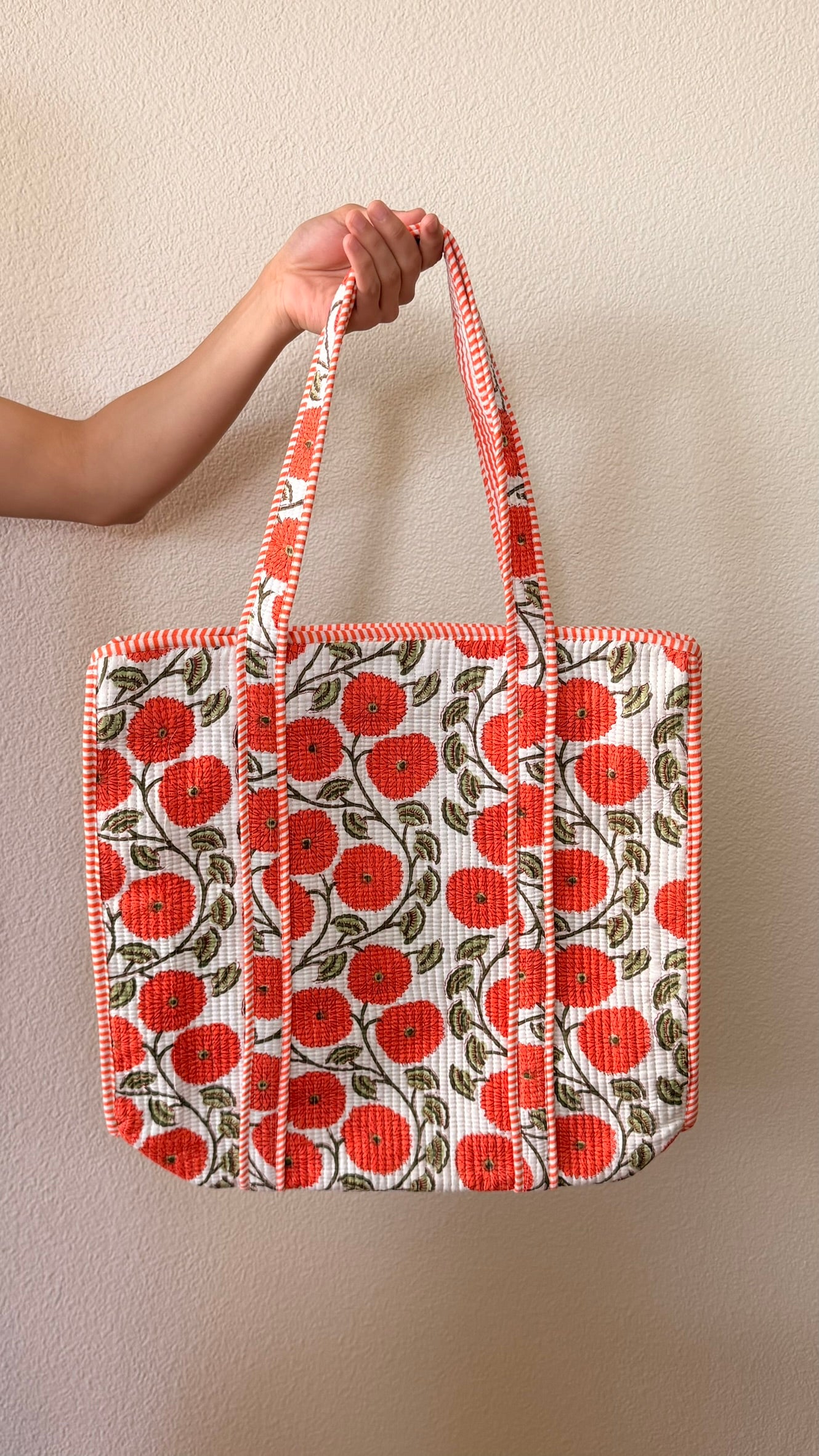 Hand-block printed quilted cotton tote bag. White background with bright orange marigolds and green leaves in a vine pattern.