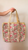 Hand-block printed quilted cotton tote bag. Featuring crimson florals, earthy vines, and ornate paisley motifs across a warm ivory backdrop.