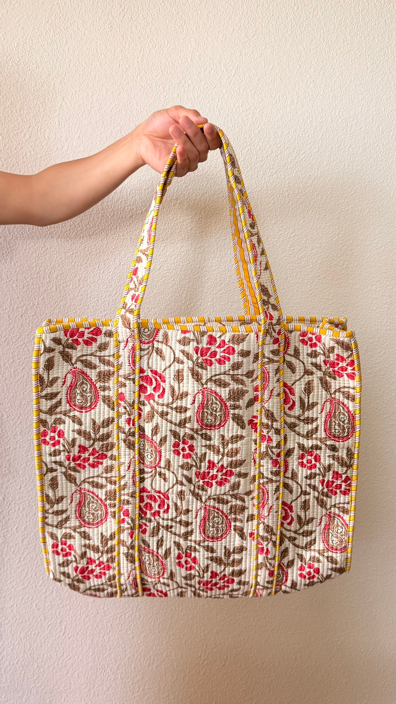 Hand-block printed quilted cotton tote bag. Featuring crimson florals, earthy vines, and ornate paisley motifs across a warm ivory backdrop.
